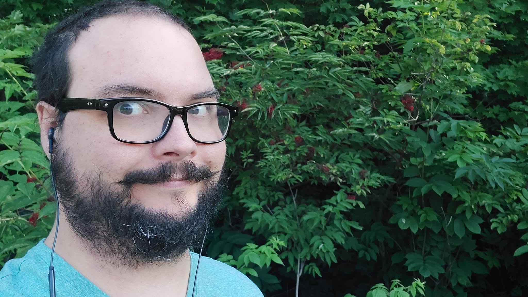 A man short hair and facial hair stands in front of a mountain ash tree